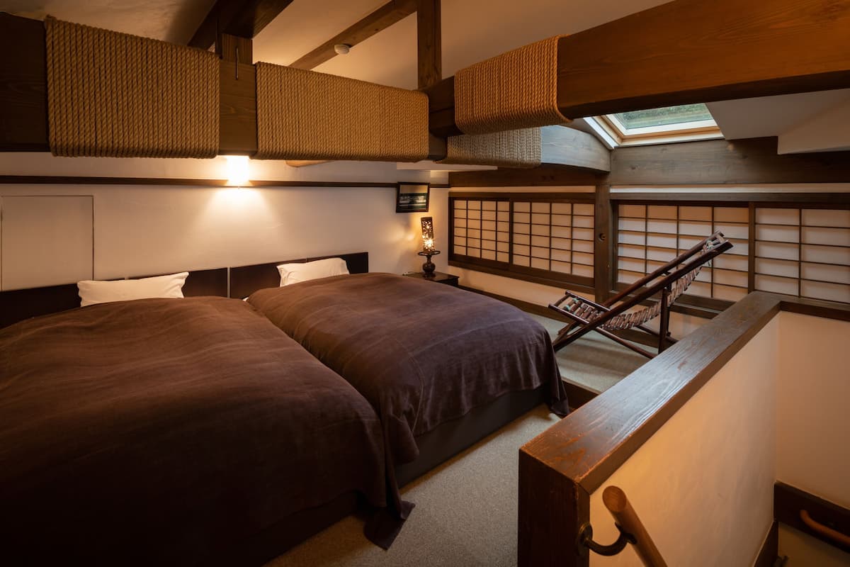 A traditional Japanese-style bedroom with two large beds, a wooden staircase, and a tatami mat wall.