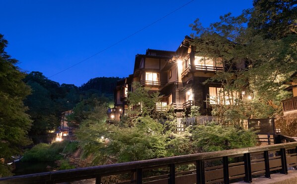 A traditional Japanese building with multiple levels and a wooden exterior, surrounded by lush greenery and a small stream. - Fujiya (Minamioguni)