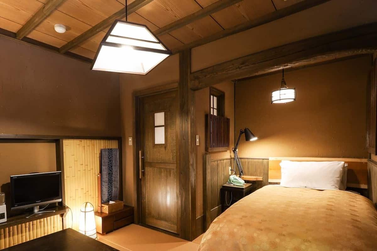 A traditional Japanese-style room with tatami flooring, a bed with a white pillow, a television on a low table, and a wooden door.