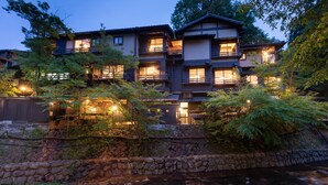 Un bâtiment de style japonais traditionnel, à plusieurs niveaux, avec des murs en pierre et une rivière au premier plan.