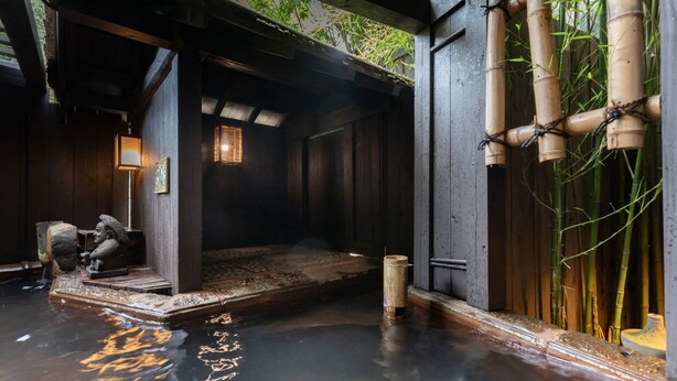 Un onsen japonais traditionnel, avec une structure en bois, un bassin en pierre et des plantes de bambou.