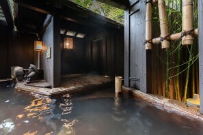 Un onsen japonais traditionnel, avec une structure en bois, un bassin en pierre et des plantes de bambou.
