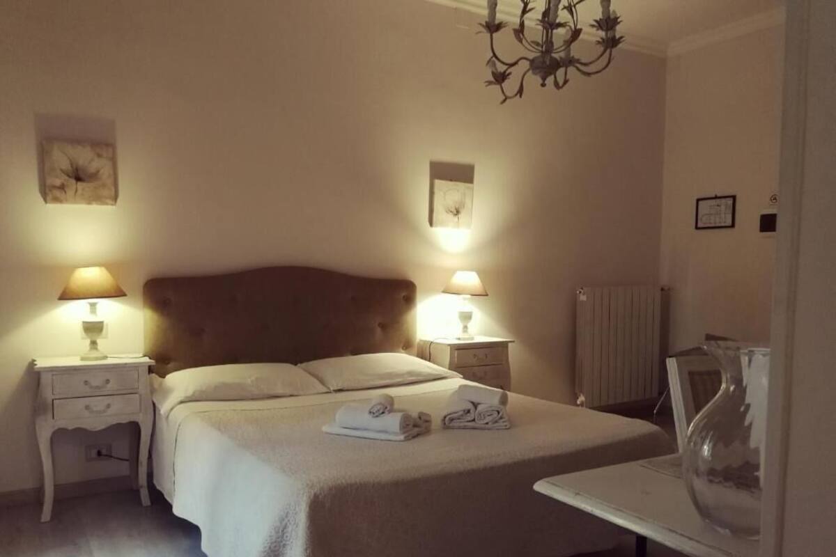 A bedroom with a large bed, two bedside lamps, a radiator, and a vase on a table.