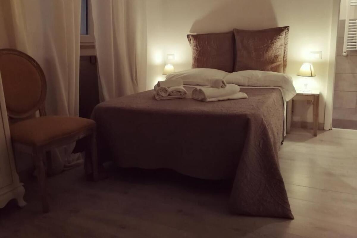 A neatly made bed with pillows and folded towels, a chair, and bedside lamps.
