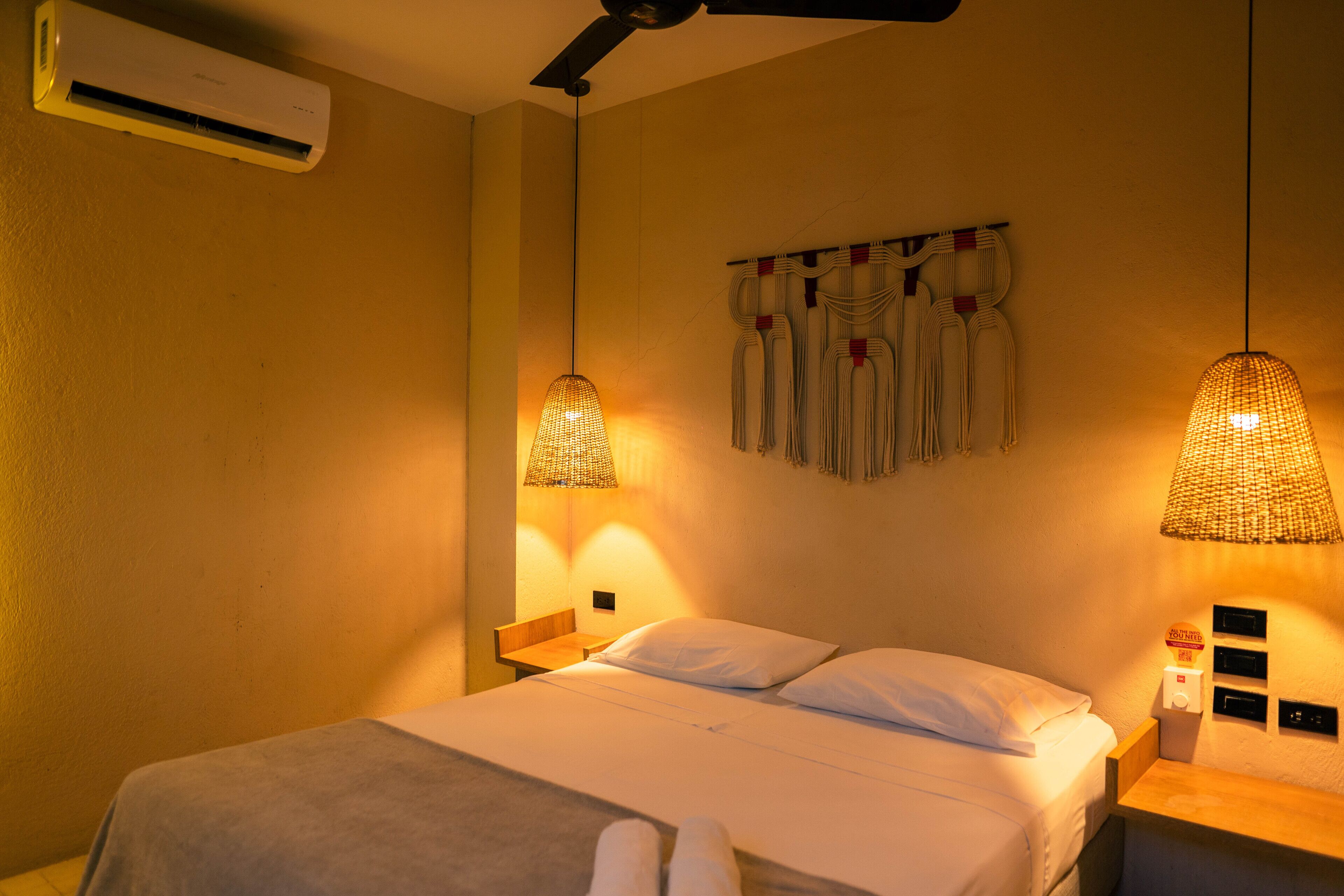 A hotel room with a bed, bedside lamps, an air conditioner, and a wall-mounted towel rack.