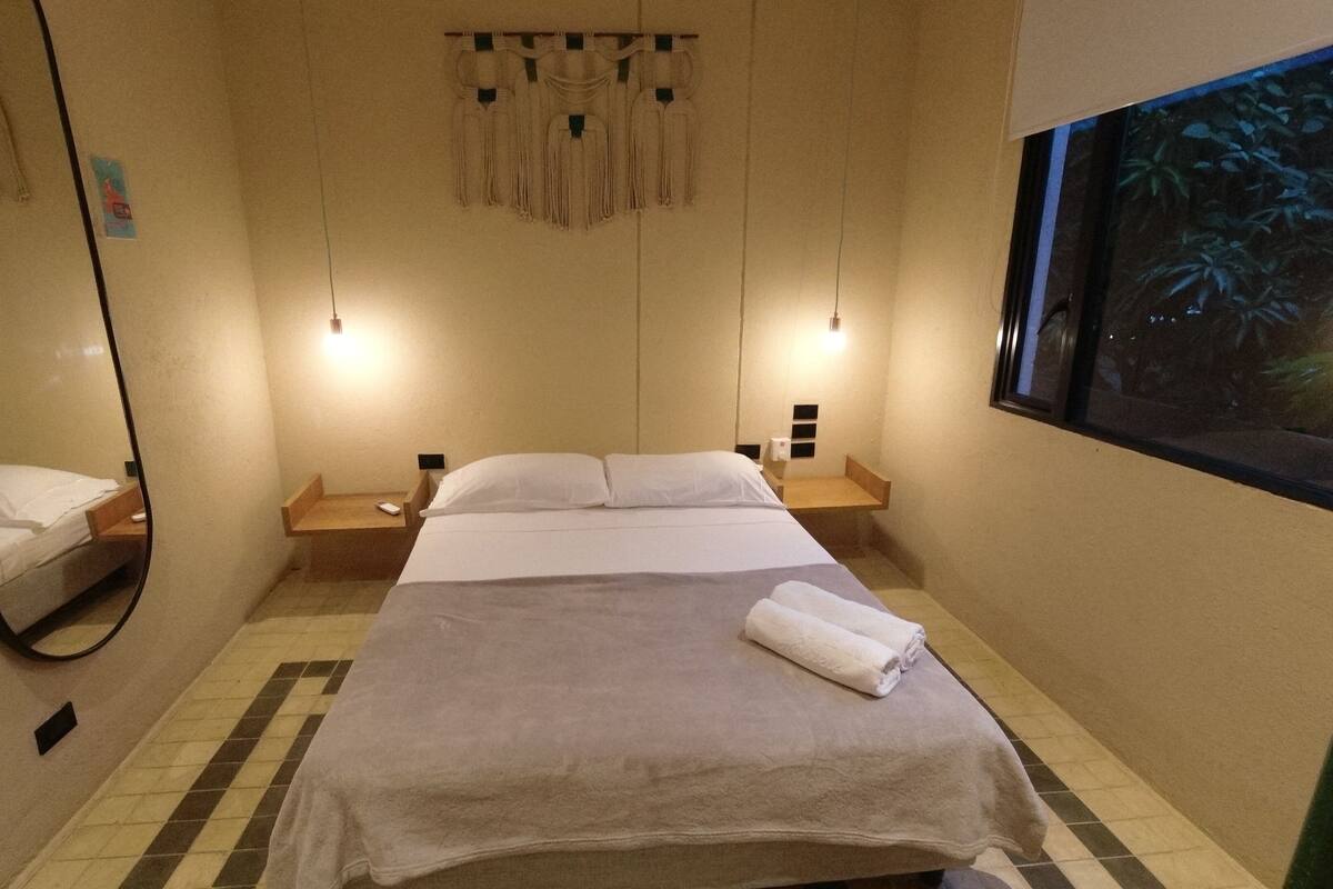 Ein Hotelzimmer mit einem Bett, einem großen Spiegel, einem Nachttisch und einer wandmontierten Lampe.