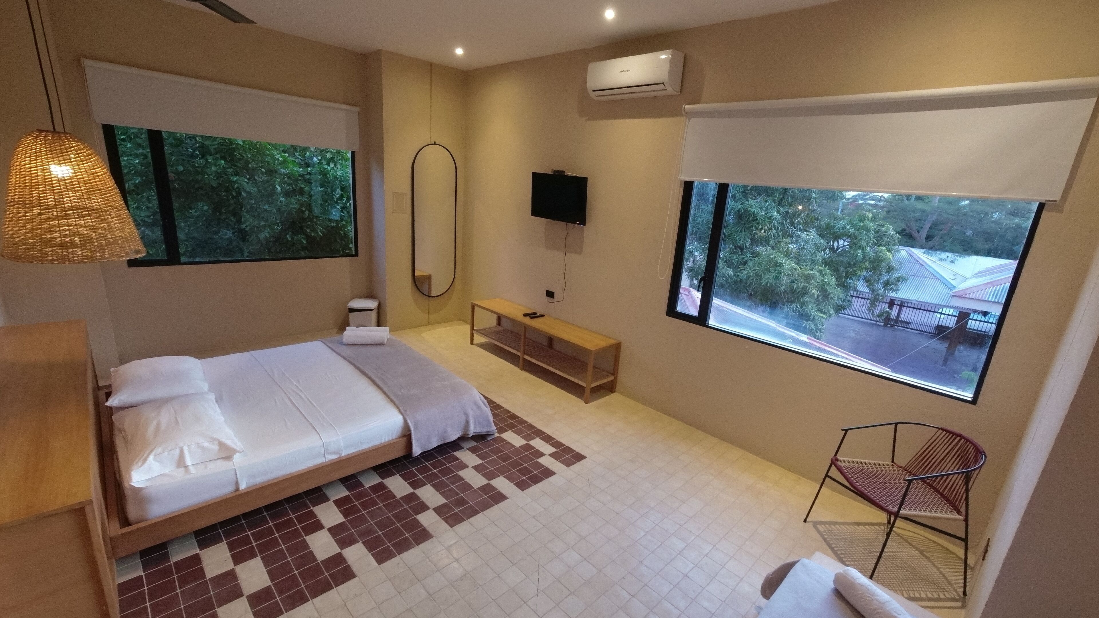 A modern bedroom with a bed, a bench, a TV, and a window with a view of trees.