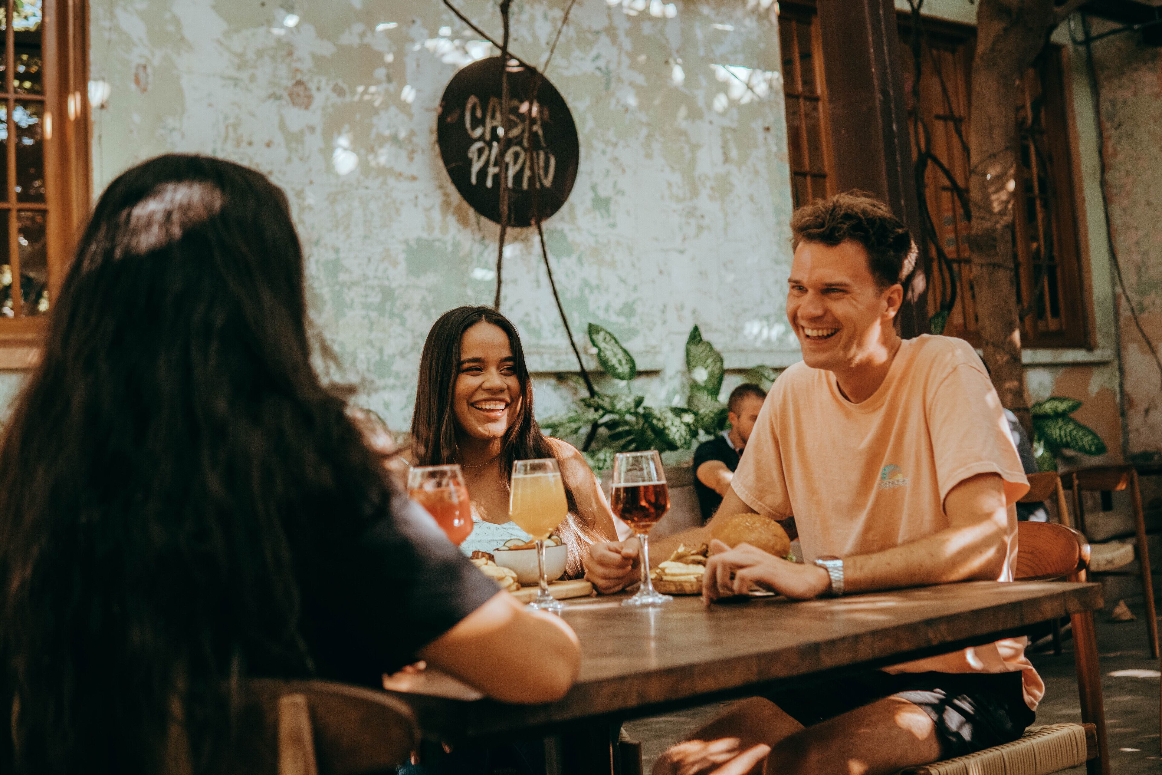 A group of people sitting around a wooden table in a rustic setting with a sign that reads "COSTA PAPU".
