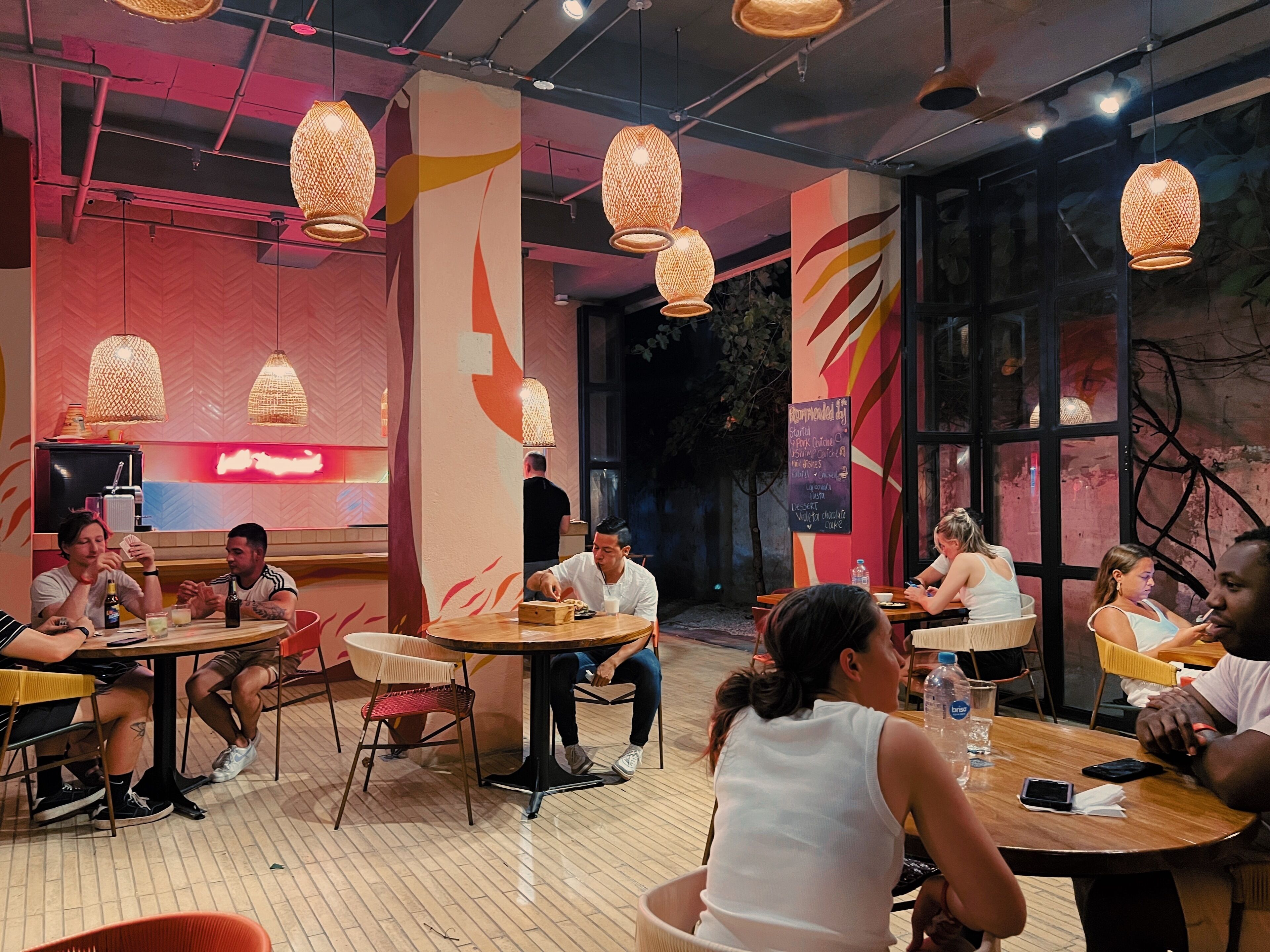 Un restaurante con mesas y sillas redondas, luces colgantes y una pizarra con el menú.