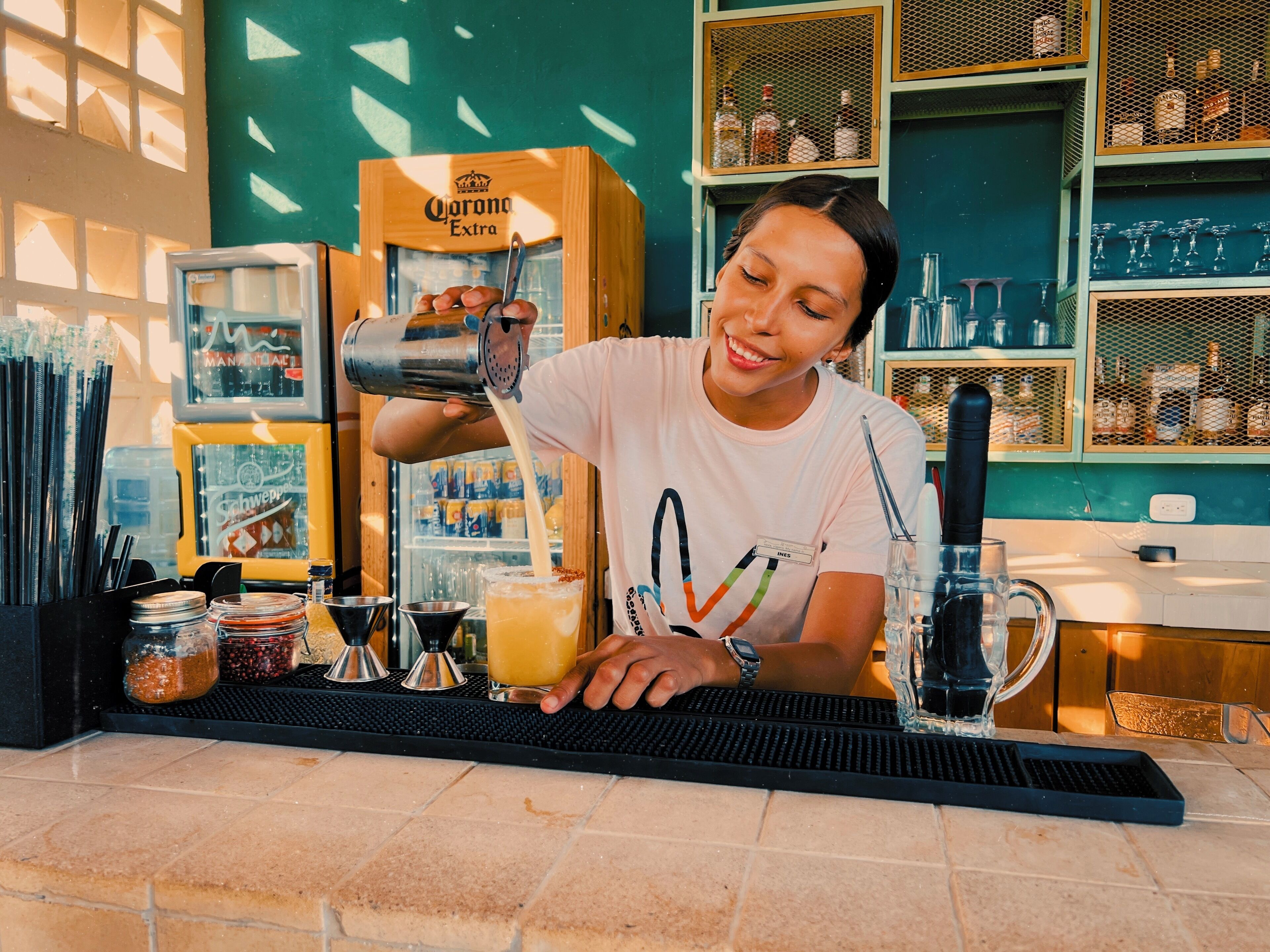 Ein Barista bereitet ein Getränk an der Theke zu, im Hintergrund steht eine Kiste Corona Extra.
