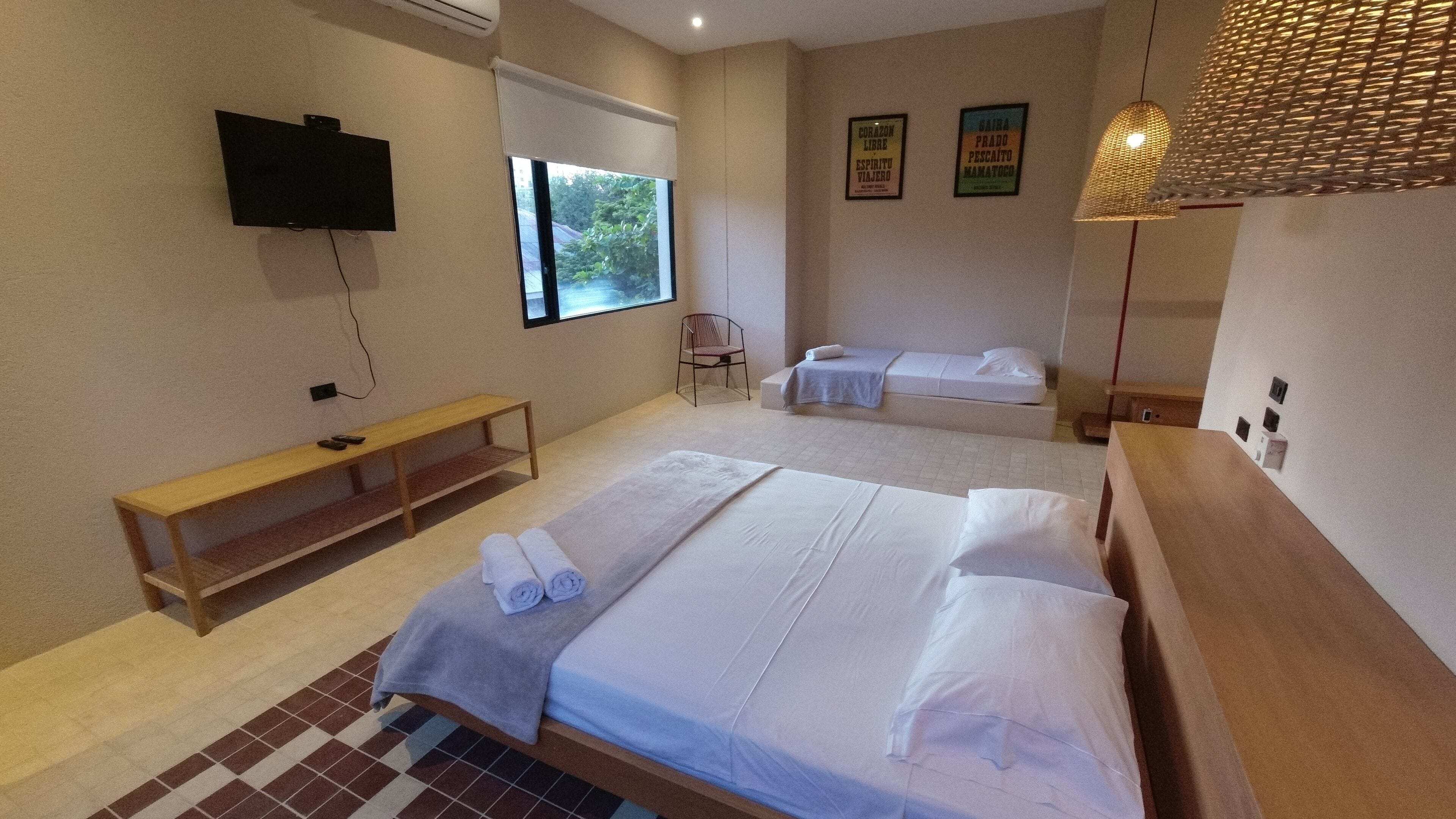 A hotel room with a large bed, a bench, a TV, and a window with a view of greenery.