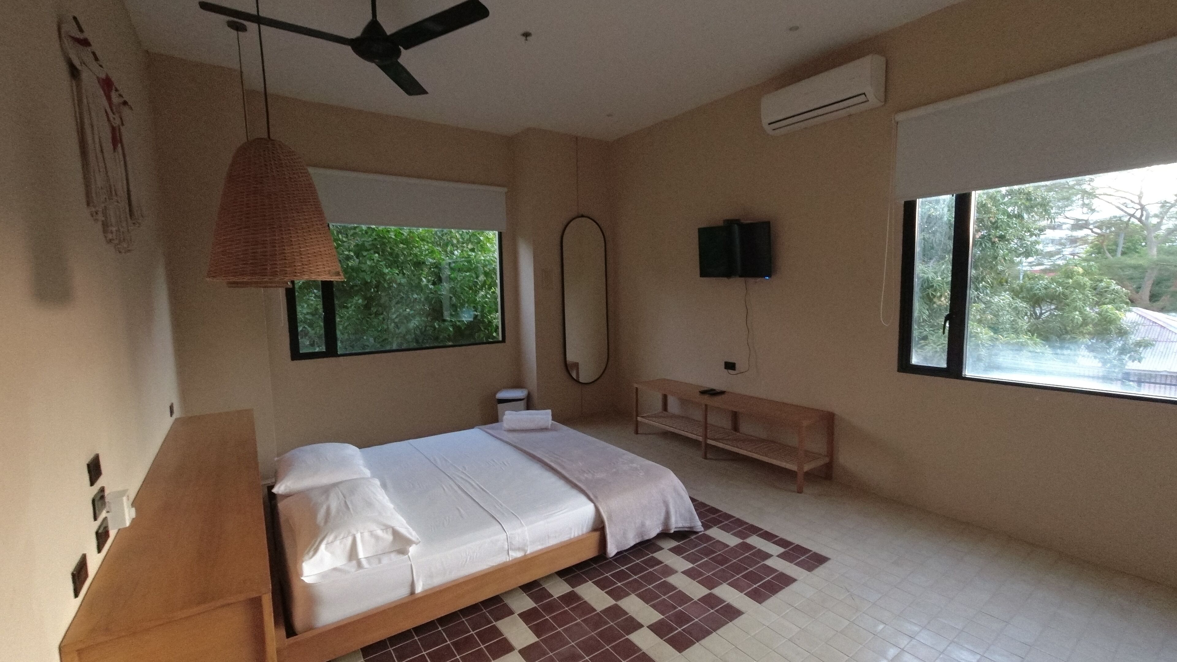 A bedroom with a bed, a ceiling fan, a TV, a window, and a mirror.