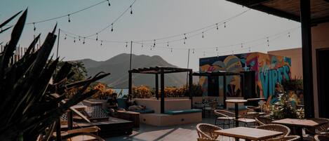 An outdoor patio with wicker furniture, string lights, and a colorful mural.