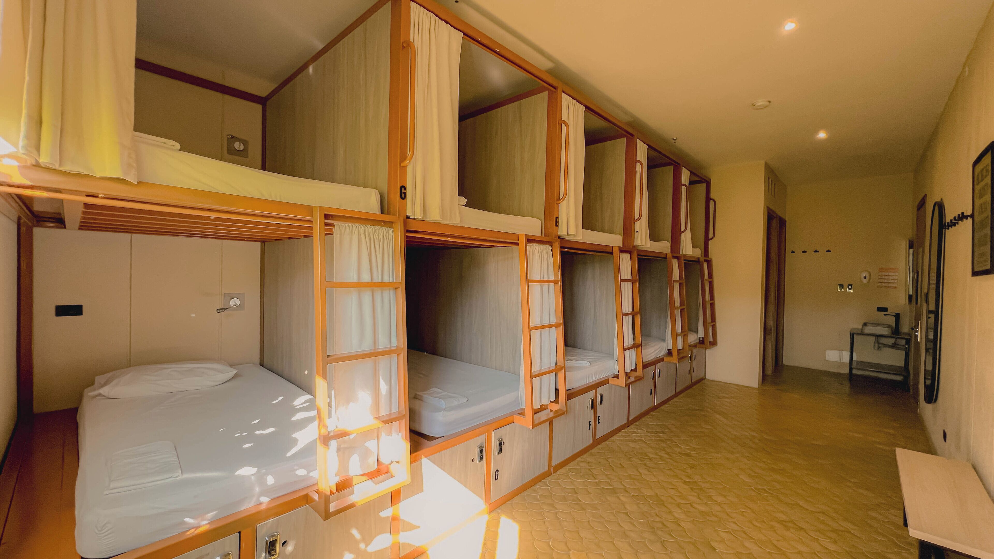 Habitación de hotel con literas, una mesita y un baño con lavamanos y espejo.