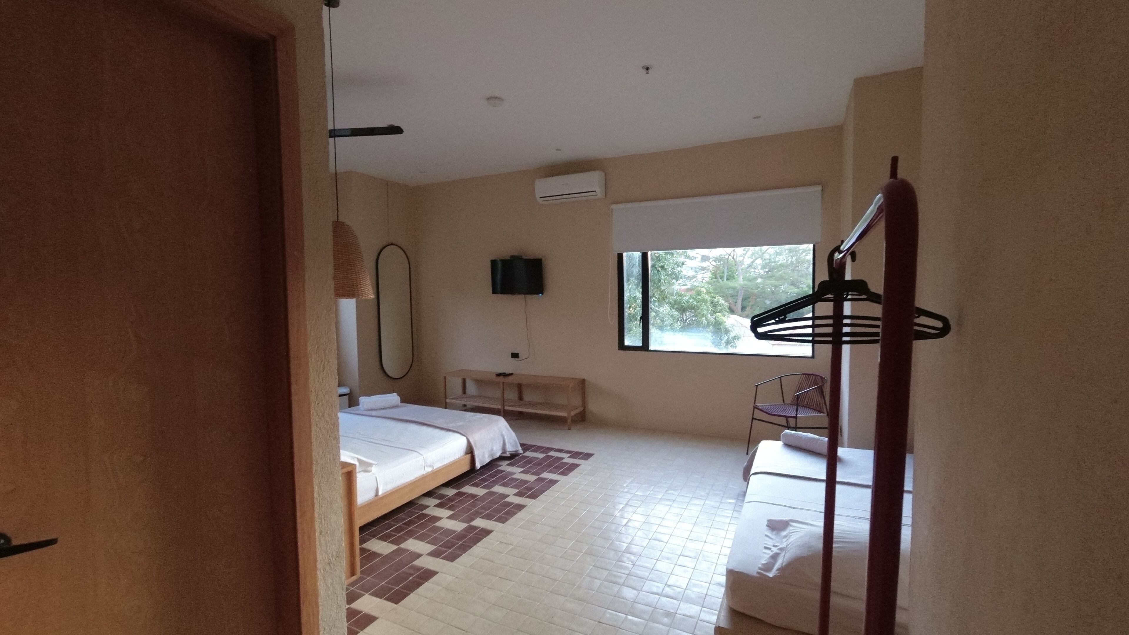 A hotel room with two beds, a TV, a window, and a hanging clothes rack.