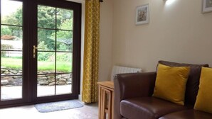 A living room with a brown leather sofa, yellow cushions, a wooden side table, and a glass door leading to a garden. - Callestock Courtyard (Truro)