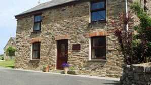 A stone building with a central entrance, two windows on the upper floor, and a small porch area with potted plants. - Callestock Courtyard (Truro)