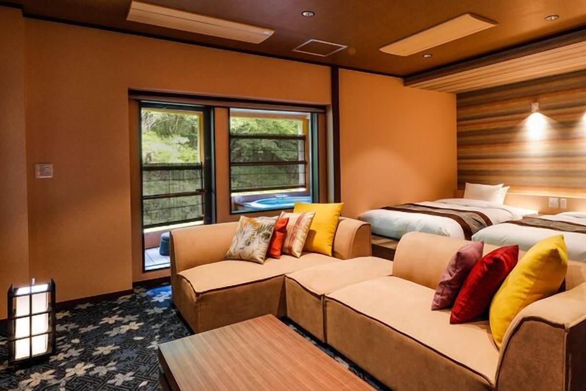 Une chambre d’hôtel moderne avec un canapé, deux lits, une fenêtre donnant sur un beau paysage et une tête de lit en bois.