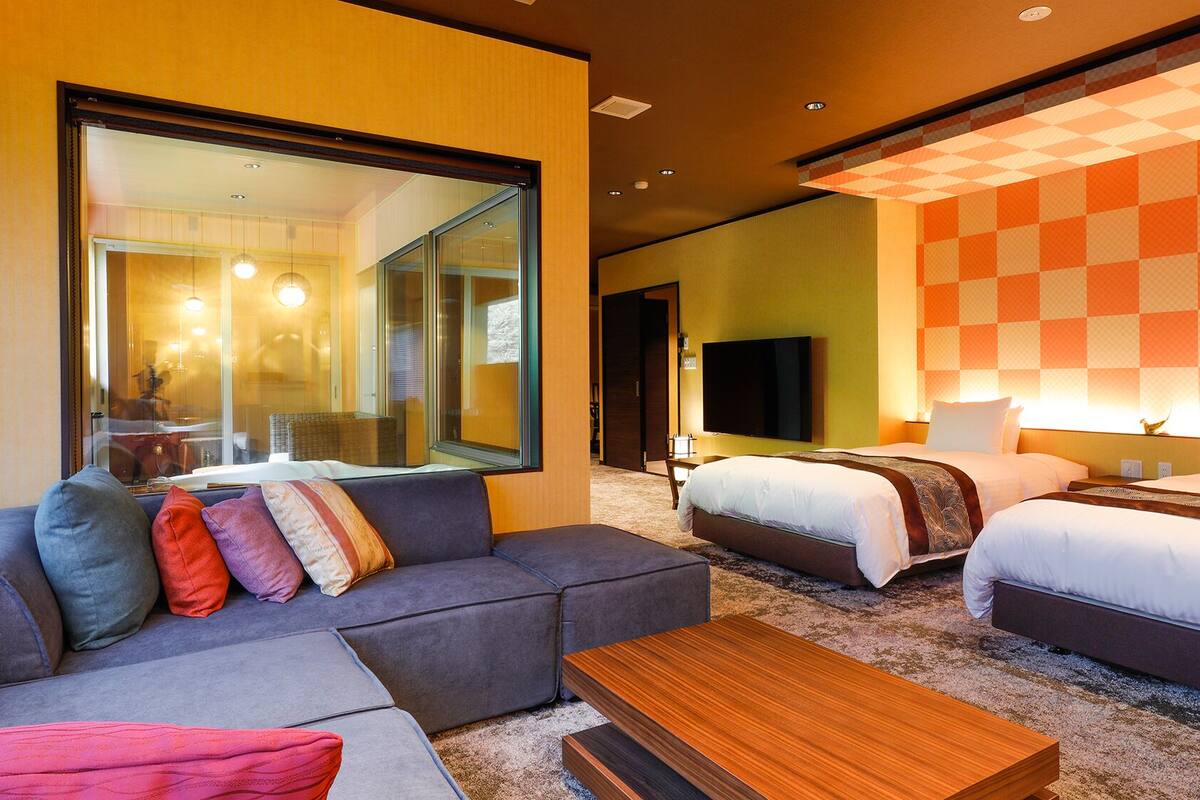 Une chambre d’hôtel avec un canapé, deux lits, une télévision et un grand miroir.