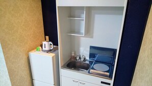 A compact kitchenette with a refrigerator, a sink, and a small countertop with a kettle and soap dispenser. - White Beachi inn Ishikawa (Uruma)