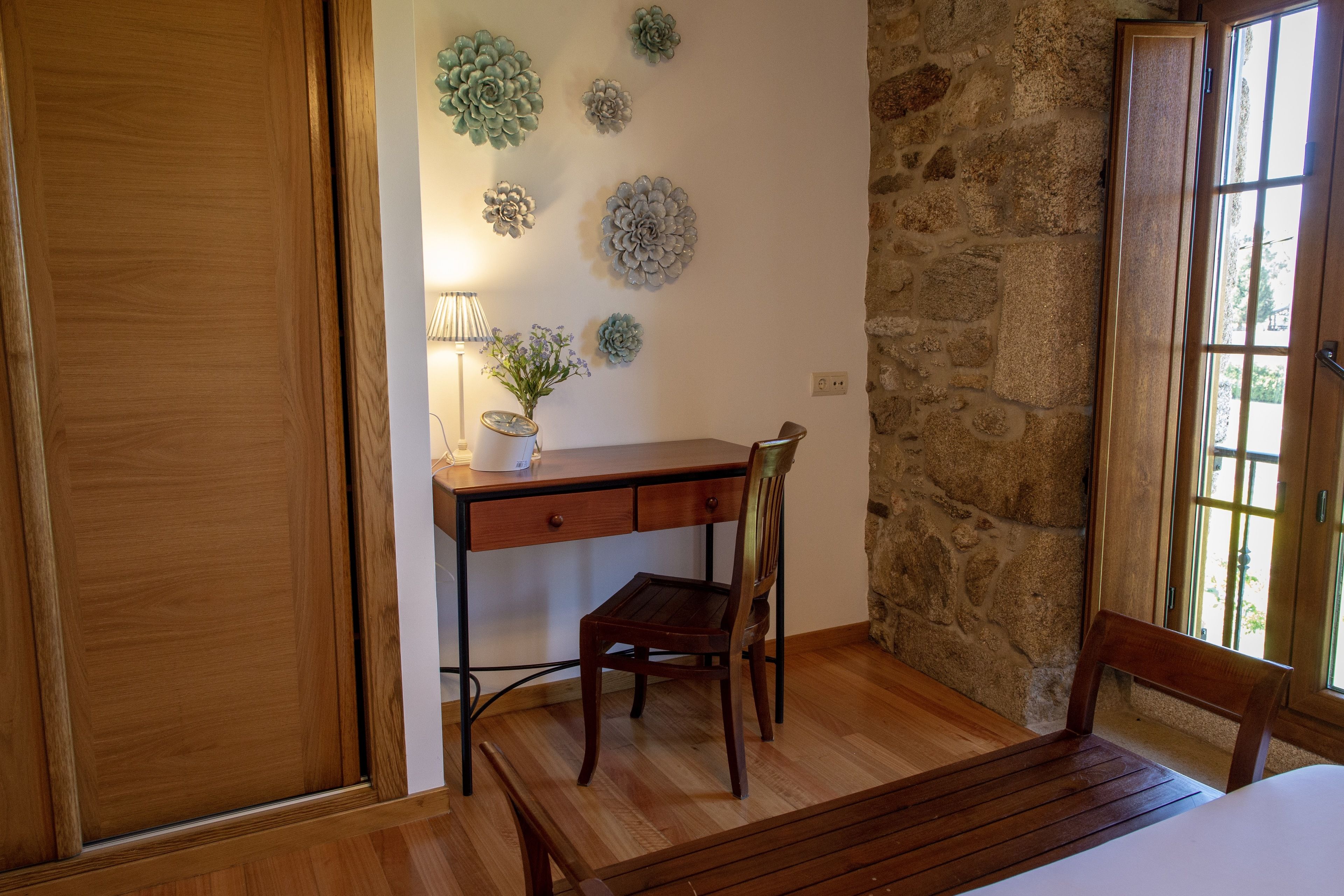 A wooden desk with a chair, a lamp, and wall decorations in a room with stone walls and a wooden floor.