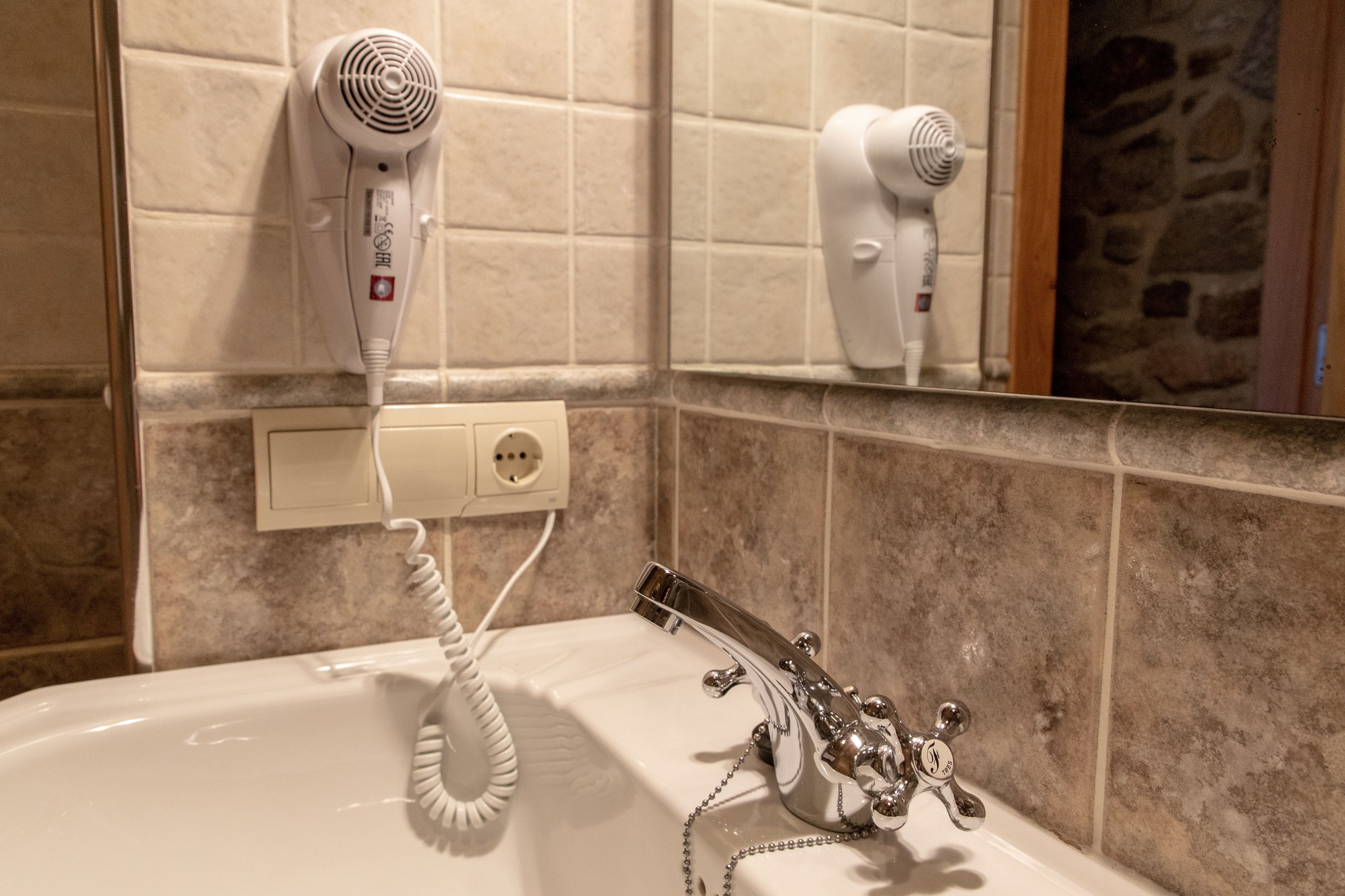 A bathroom with a bathtub, a hairdryer mounted on the wall, and a mirror reflecting the hairdryer.
