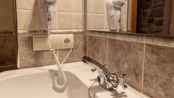 A bathroom with a bathtub, a hairdryer mounted on the wall, and a mirror reflecting the hairdryer.