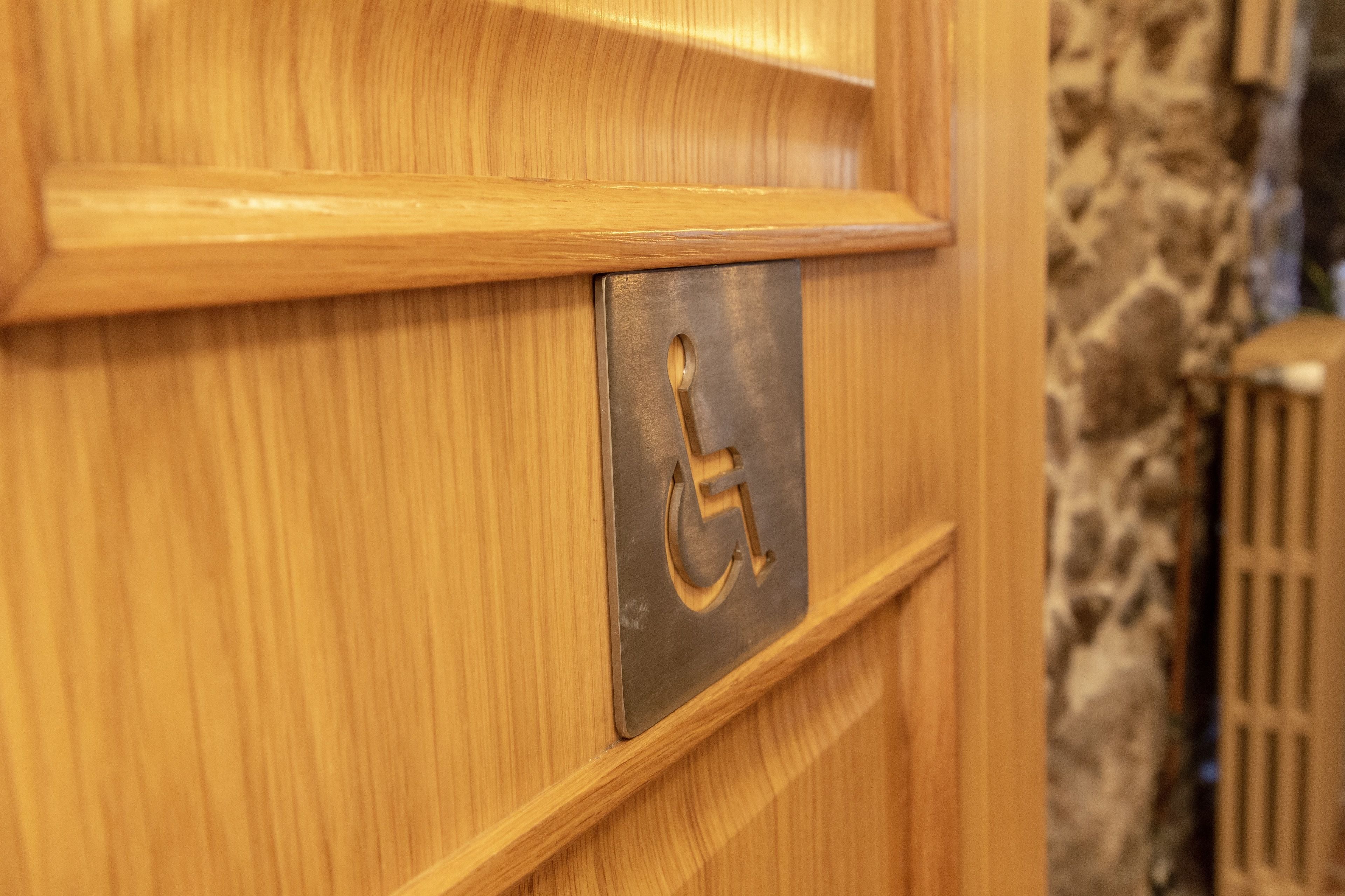 Una puerta de madera con el símbolo de accesibilidad para personas con discapacidad y una placa de metal.