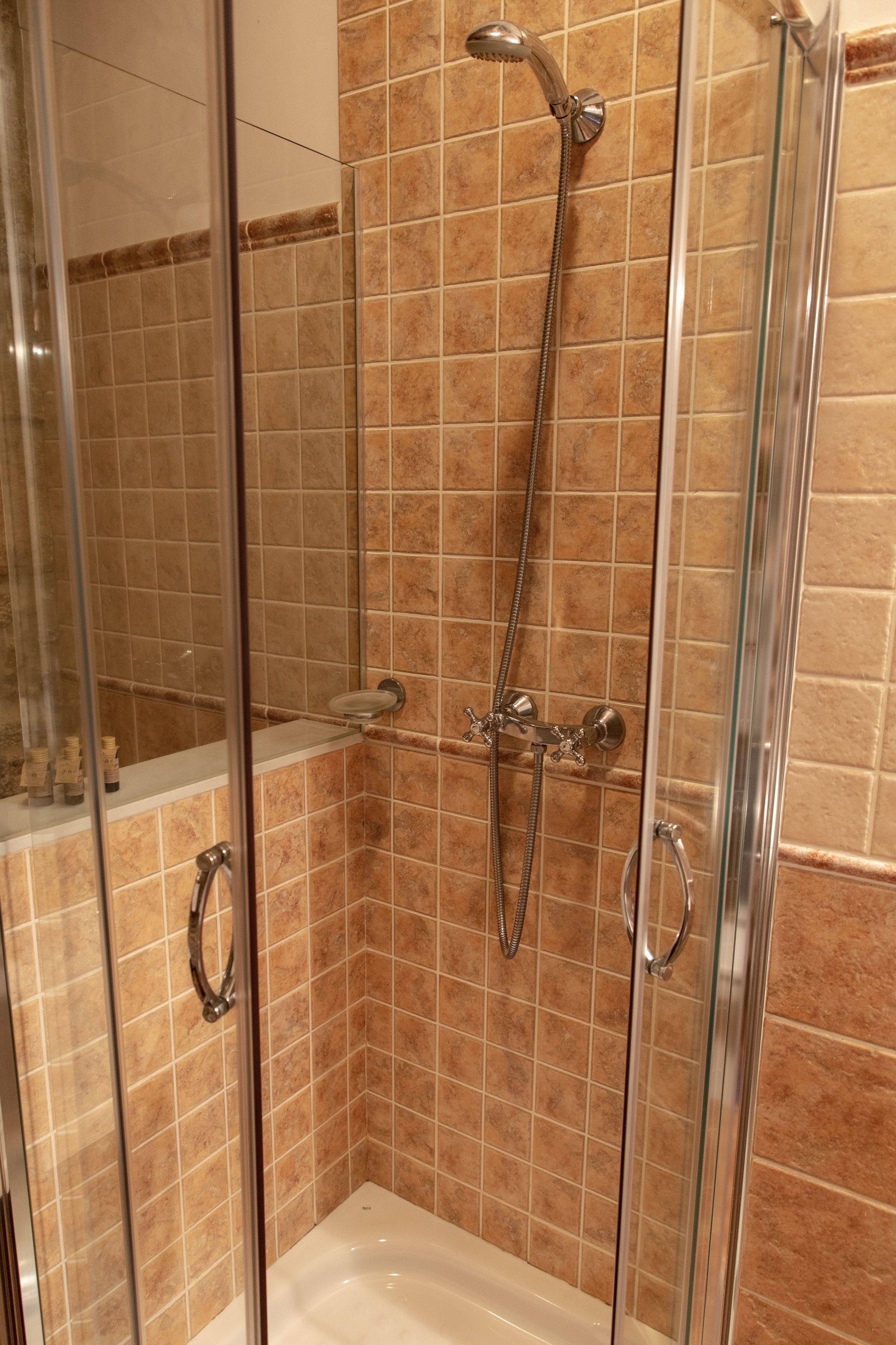 Cabina de ducha con paredes de vidrio, cabezal de ducha de mano y rociador de mano.