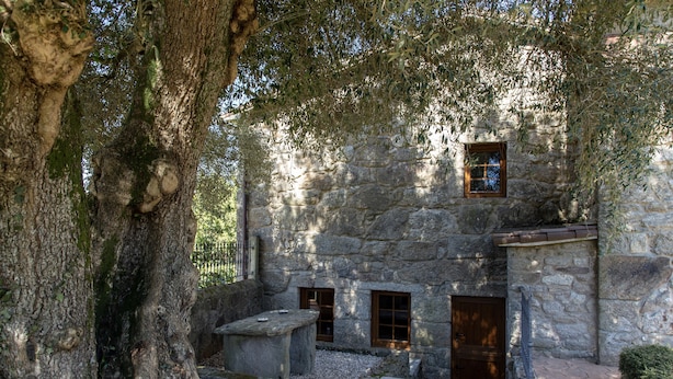 Un edificio de piedra con un banco rústico de piedra y un ventanal pequeño.