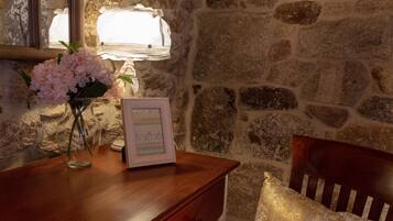 A wooden desk with a vase of flowers, a framed picture, and a lamp against a stone wall.