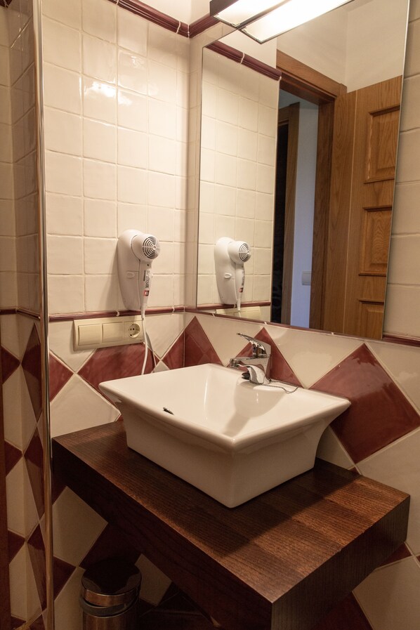 A bathroom with a white sink, two hair dryers mounted on the wall, and a mirror reflecting the room. - Casa Rural as Bentinas (Ames)
