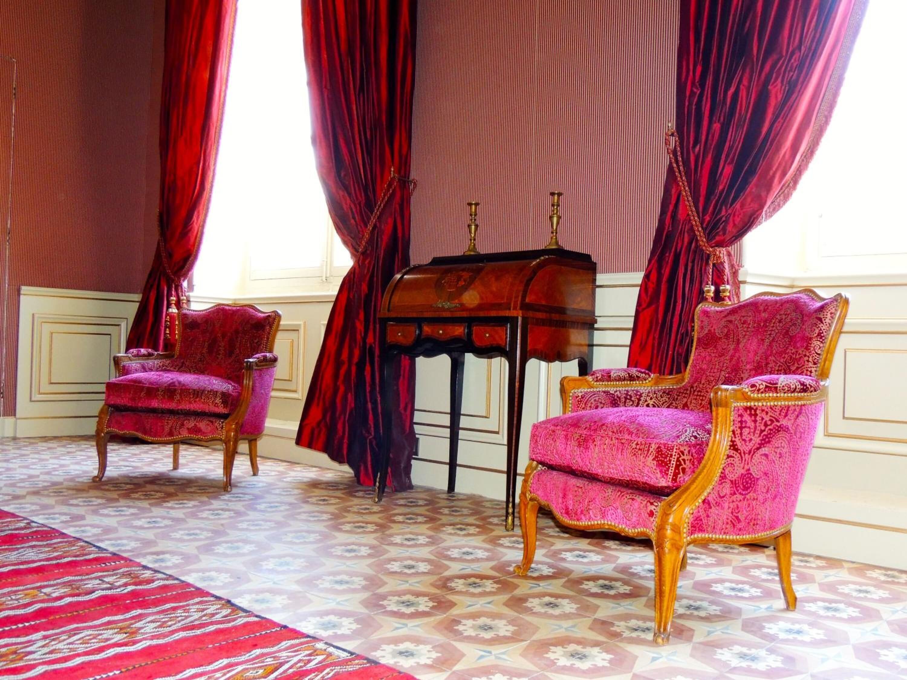 A room with two ornate chairs, a small wooden table, and a patterned carpet.