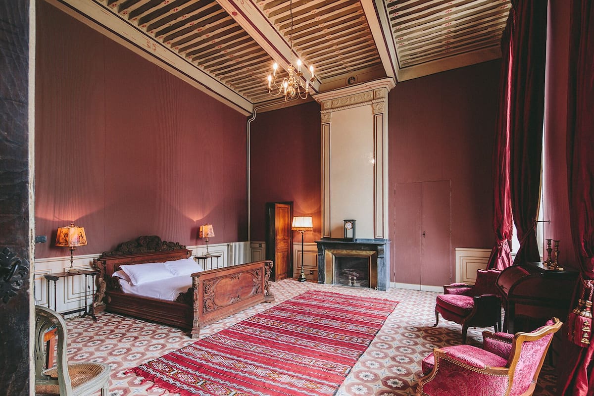 A room with a large bed, a fireplace, a red carpet, and a chandelier.