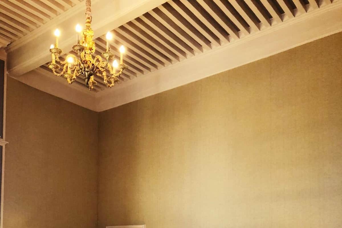 A spacious bedroom with a large bed, two bedside tables with lamps, a wooden floor, and a chandelier.