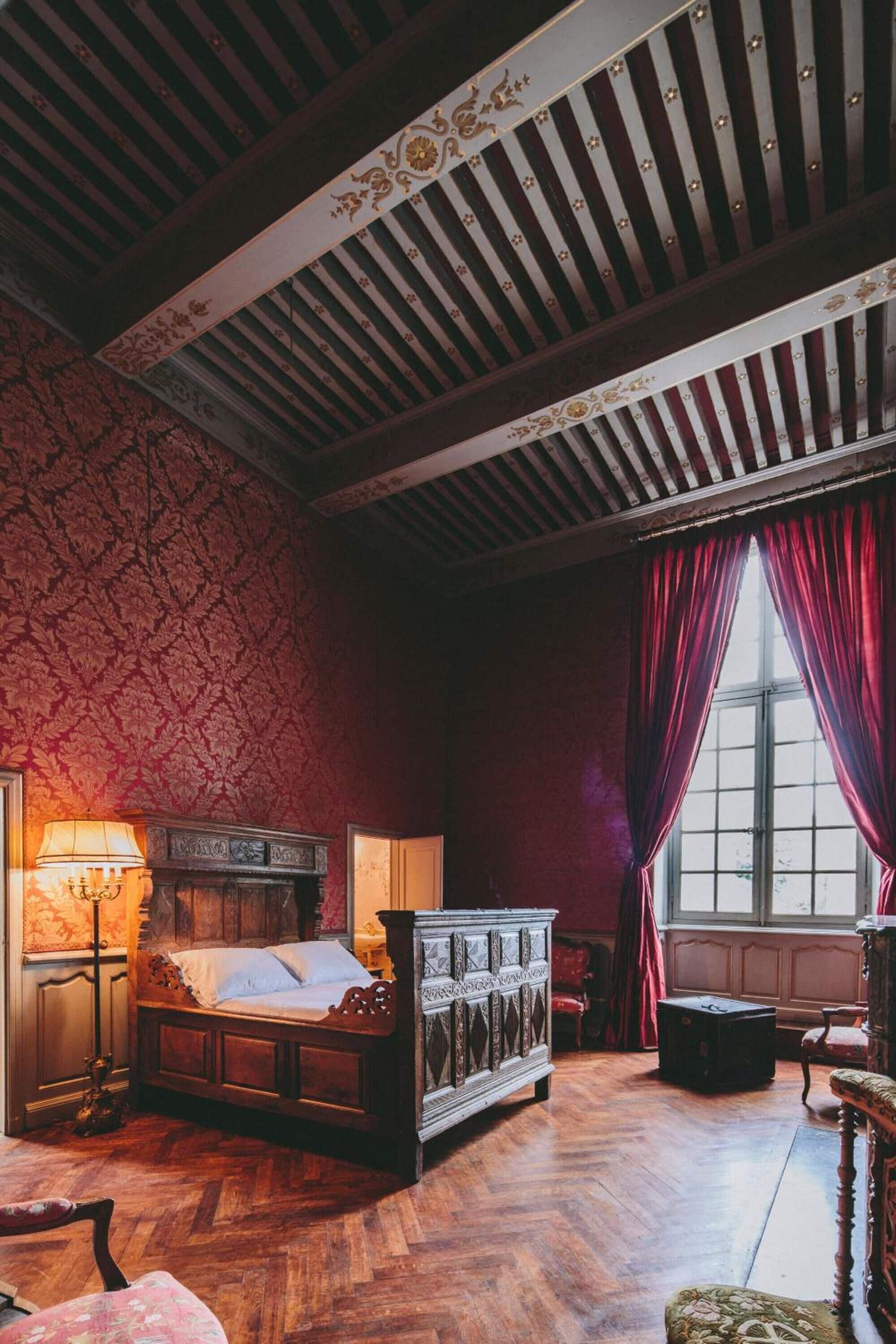 A traditional bedroom with a wooden bed, a nightstand, a lamp, and a window with curtains.