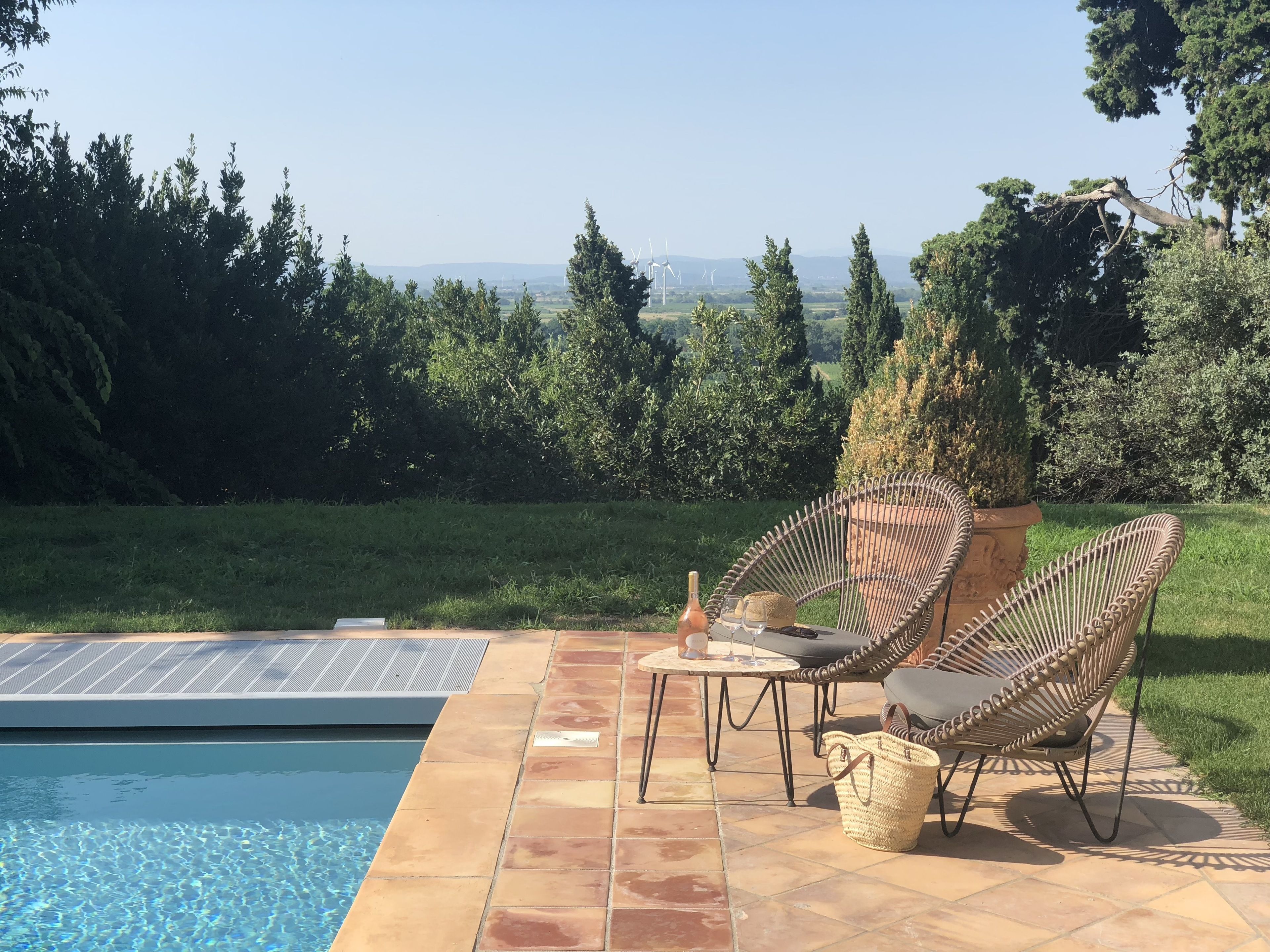 Un espace aménagé au bord de la piscine, offrant une vue sur des éoliennes au loin, et entouré de verdure.
