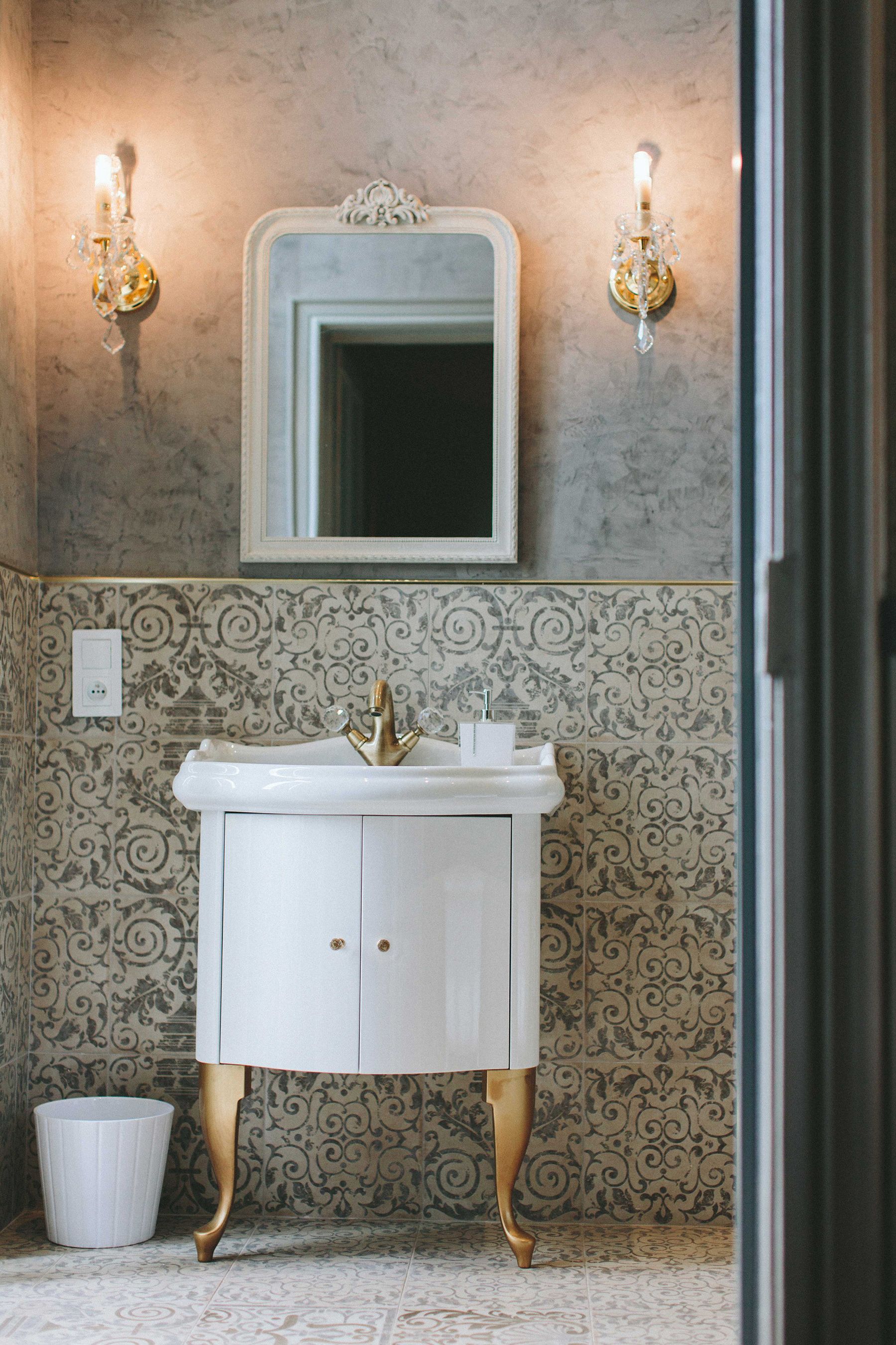 A bathroom with a white sink, gold faucet, and ornate wall sconces.