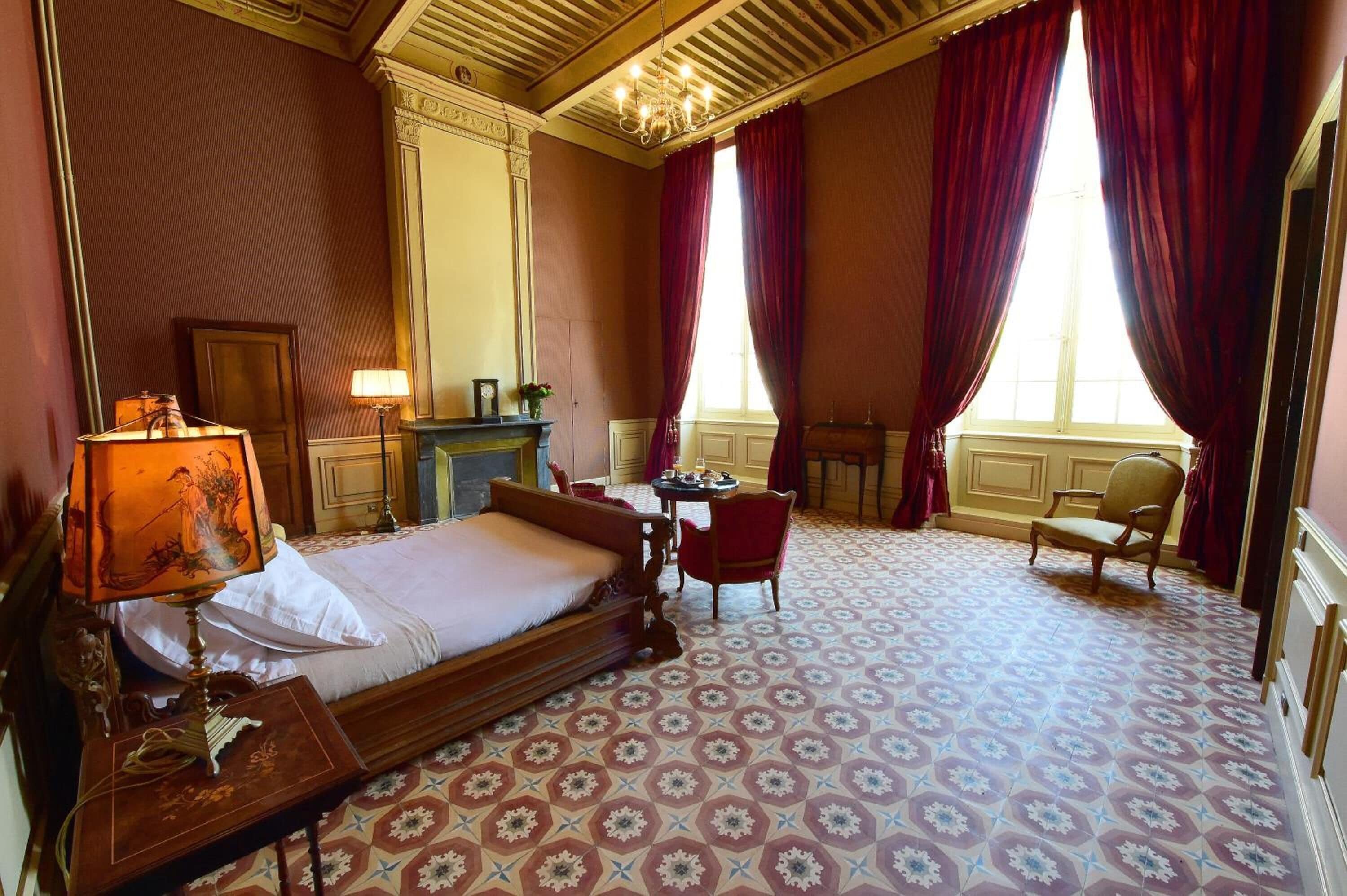 Habitación de hotel con una cama grande, un escritorio, dos sillas, una chimenea y un ventanal con cortinas.