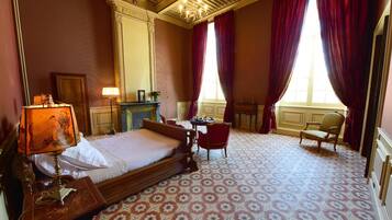 Habitación de hotel con una cama grande, un escritorio, dos sillas, una chimenea y un ventanal con cortinas.