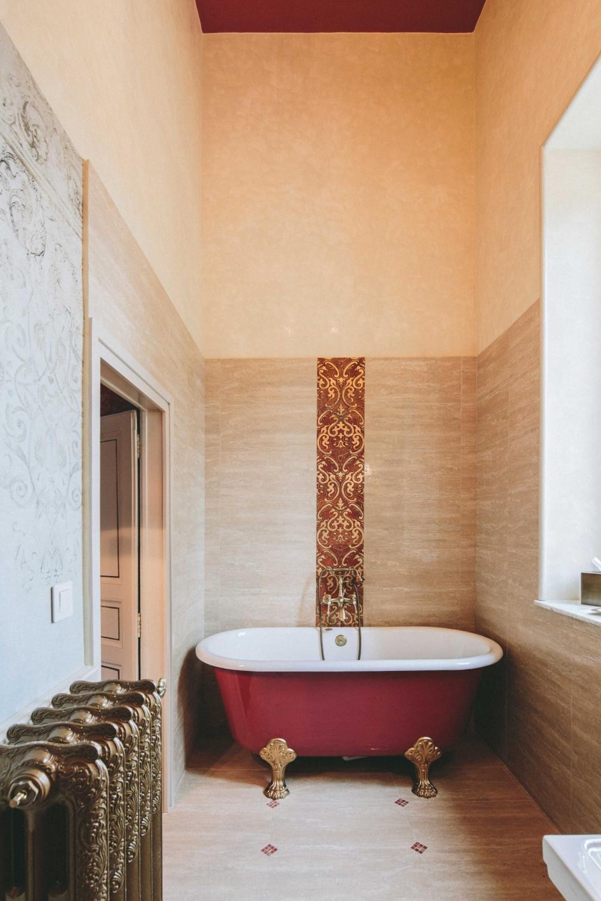 Une petite salle de bain avec une baignoire rouge, un radiateur et un papier peint à motifs.