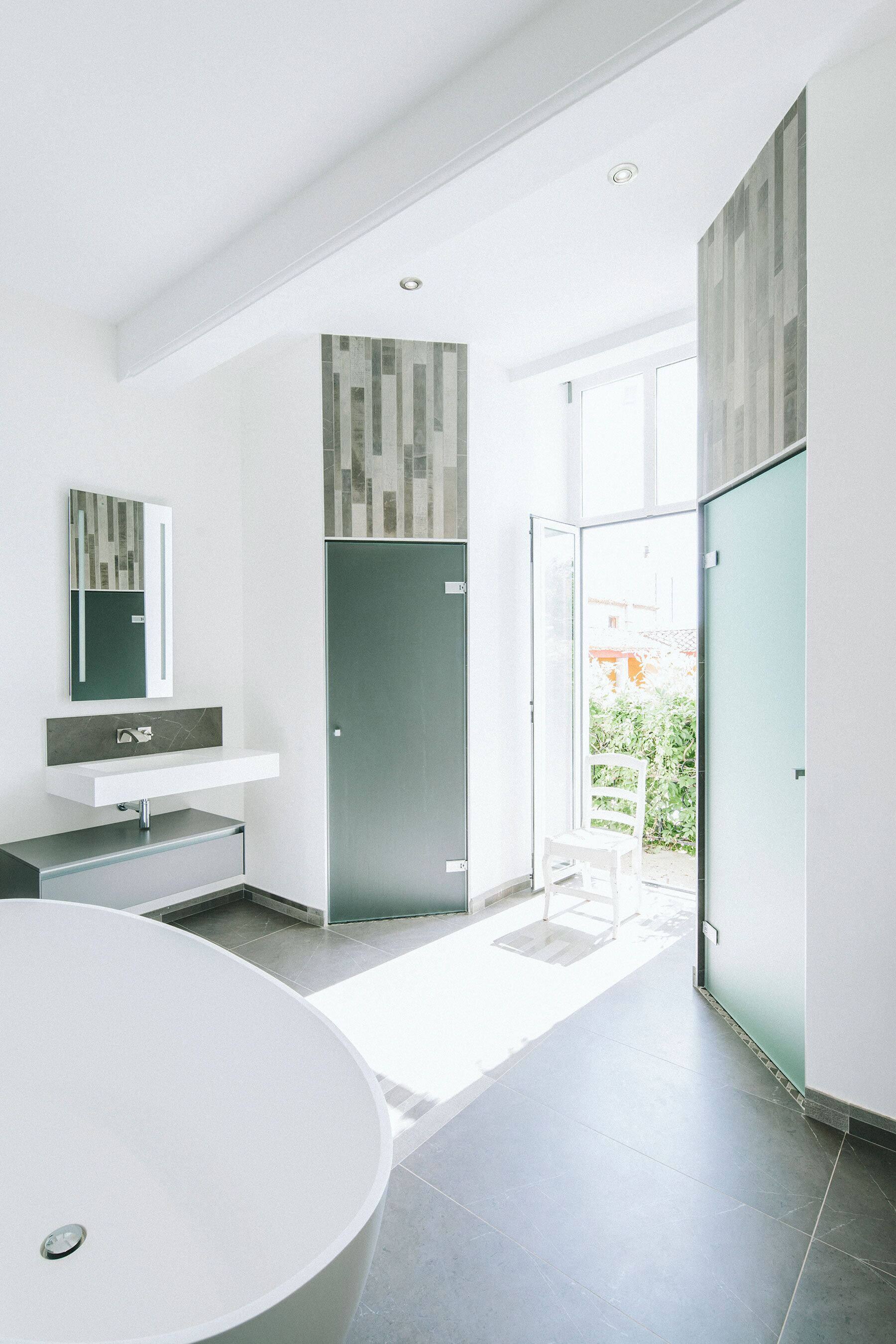 A modern bathroom with a large bathtub, a vanity with a mirror, and a door leading to a balcony.