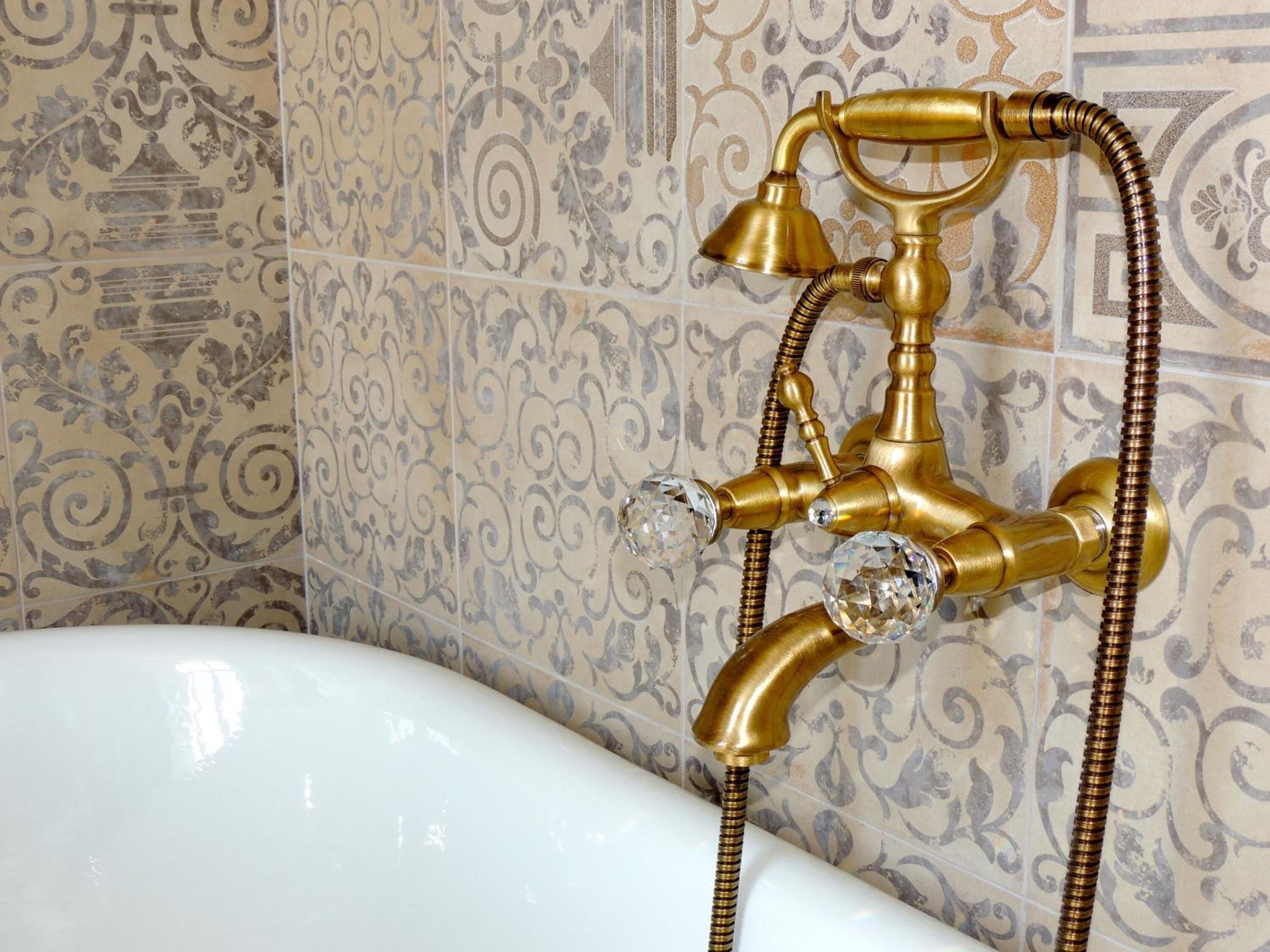 Un baño con una bañera blanca, un cabezal de ducha de latón y baldosas con diseño.