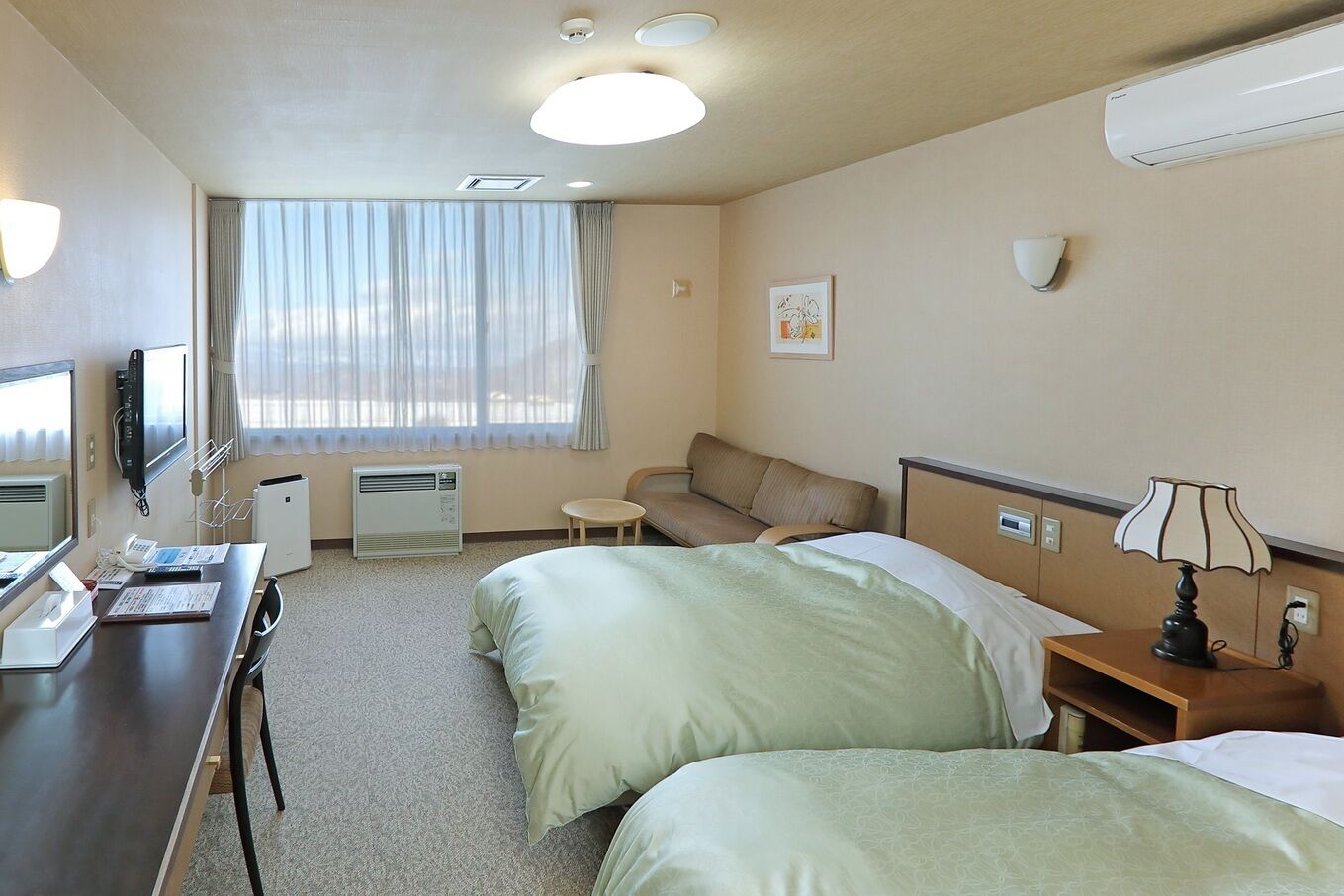 Habitación de hotel con escritorio, dos camas, un sofá, televisor, calefacción y una ventana con cortinas.