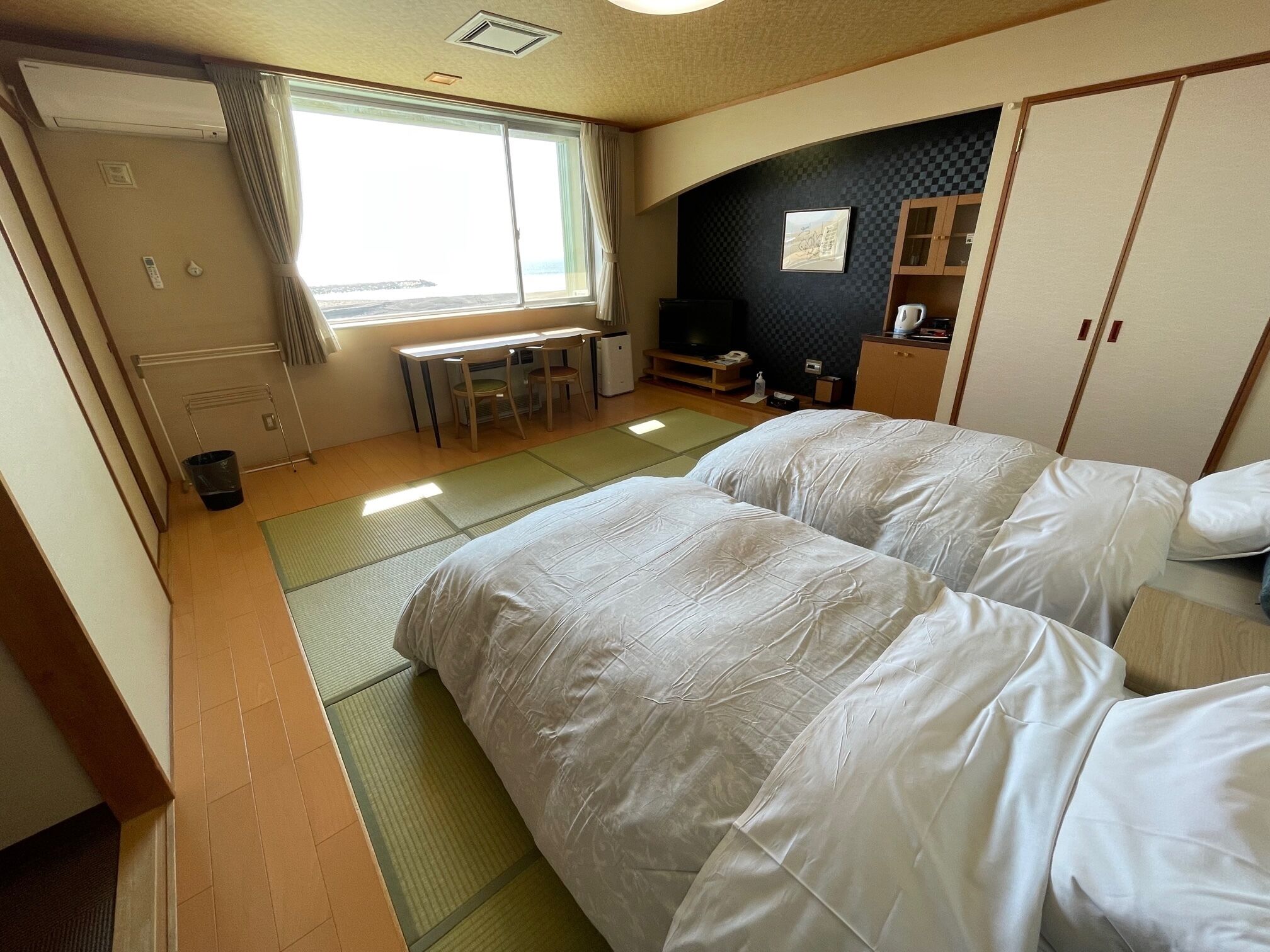 A hotel room with tatami mats, a bed, a desk with chairs, a TV, and a wardrobe.