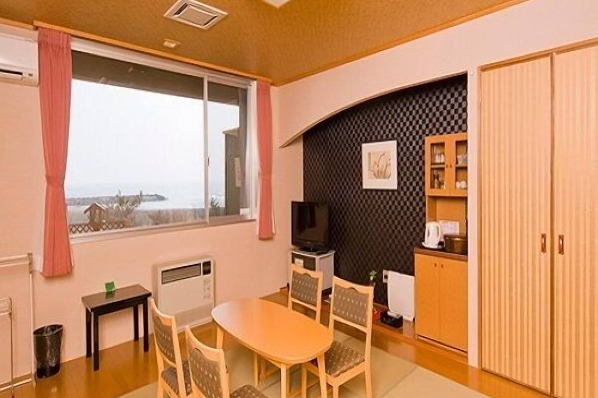 Una habitación con una mesa de comedor, sillas, un televisor, un armario y vistas por una ventana.