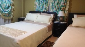 Una habitación de hotel con una cama grande, dos mesitas de noche, una lámpara y cortinas con estampado floral.