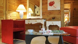 Een knus vertrek met houten wanden, een rode bank, een glazen salontafel en een witte schoorsteen.