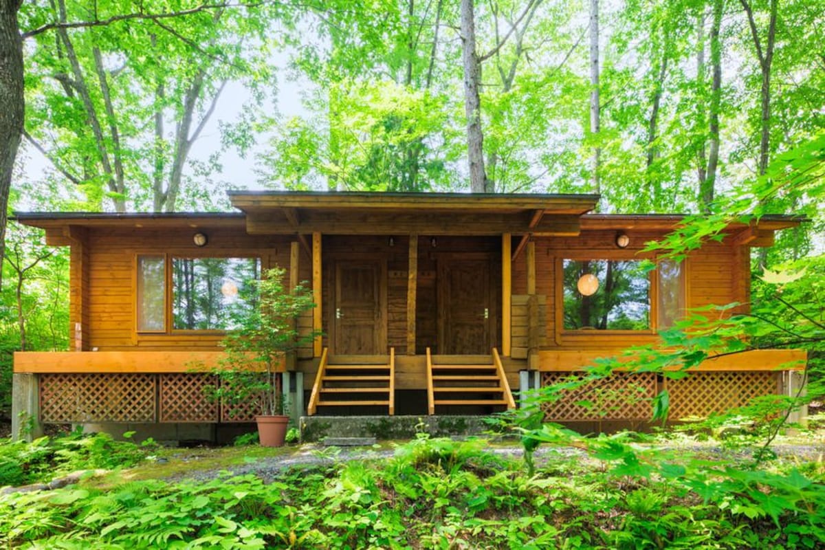 A wooden cabin with a front porch, large windows, and a staircase leading to the entrance.