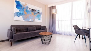 Uma sala de estar moderna com um sofá cinzento, uma mesa de centro redonda e uma área de jantar com uma cadeira e mesa.